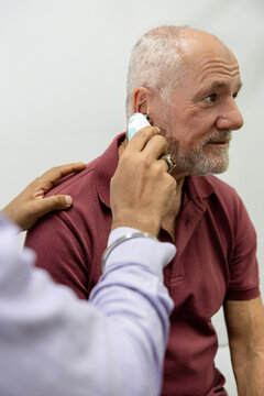 Doctor using ear thermometer on middle-aged patient