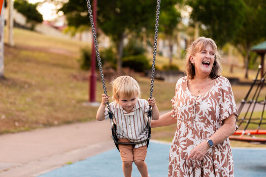 Happy grandmother playing with grandson child on swing at park on hot afternoon in Australia