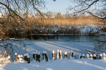Snow covers the banks of a frozen river surrounded by trees on a clear winter day in a serene landscape
