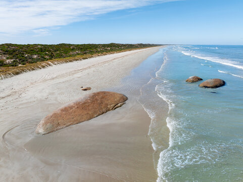 Aerial view of waves lapping against large granite boulders embedded in a sandy beach
