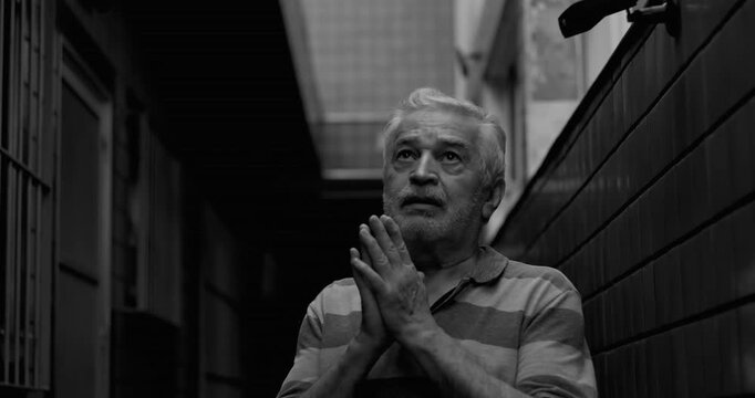 Senior man praying in narrow corridor seeking God help during difficult times, faith, hope, surrender, spiritual resilience amid hardship