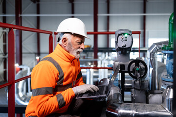 Senior engineer is monitoring smart factory machines with a laptop