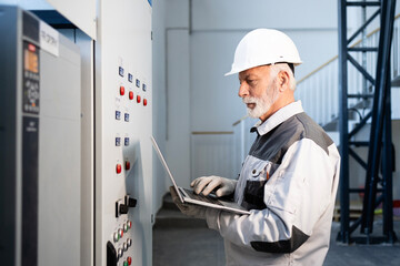 Senior engineer checking industrial control panel with laptop