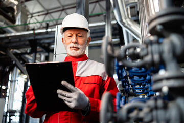 Senior engineer wearing hard hat and workwear inspecting factory equipment