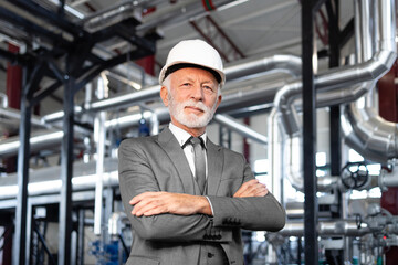 Senior engineer with hard hat arms crossed in factory