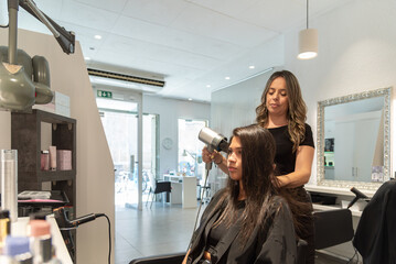 Hairdresser blow drying client's long hair in salon