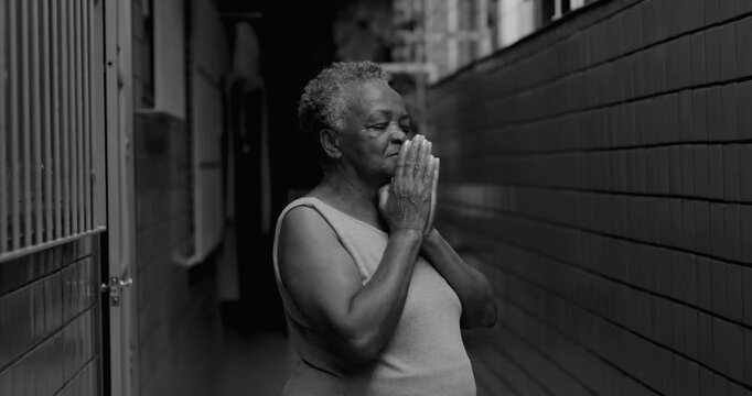 Elderly African American woman standing in narrow corridor praying quietly, eyes closed, steadfast faith, spiritual reflection, calm resilience in everyday life