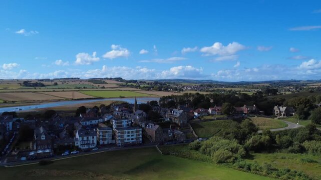 Aerial drone view flying along the village of Alnmouth in Northumberland showing buildings and roads along the river Aln and surrounding countryside