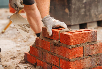 Bricklayer builder working laying red bricks and blocks on construction site
