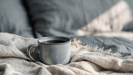 Blue-gray ceramic mug of coffee rests on a soft beige blanket on a cozy bed. Concept Blue-gray ceramic mug, Coffee on a soft beige blanket, Cozy bed, Beige blanket texture, Homey morning moment