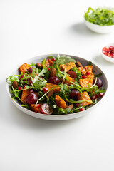 Fresh salad with roasted pumpkin and grapes on plate  light surface