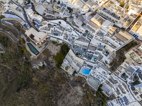 Aerial view of whitewashed buildings cascading down the volcanic cliffs, pools gleaming like jewels, a tapestry of textures and tones in the fading light, Fira, Santorini, Greece.