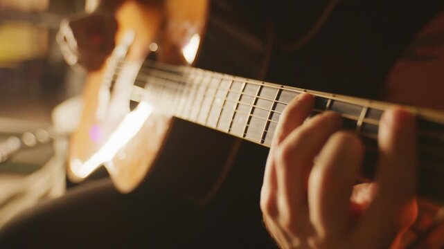 Static close-up of a hand picking guitar strings in a warm, cozy studio.