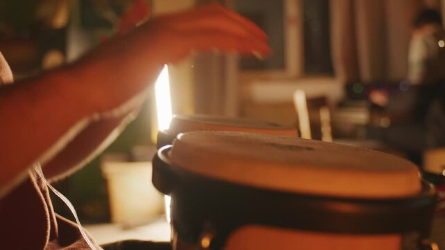 Static close-up of hands playing bongos in a cozy studio with warm lighting.