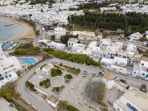 Aerial view of whitewashed buildings contrasting against the deep blue sea and clear skies, with a traditional windmill standing proudly, Paros, Paros, Greece.