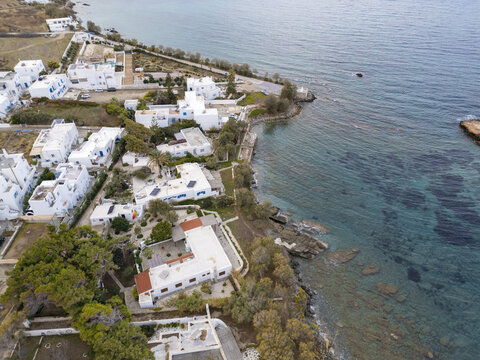 Aerial view of white buildings meeting the turquoise sea, creating a striking contrast along the coastline, Paros, Paros, Greece.