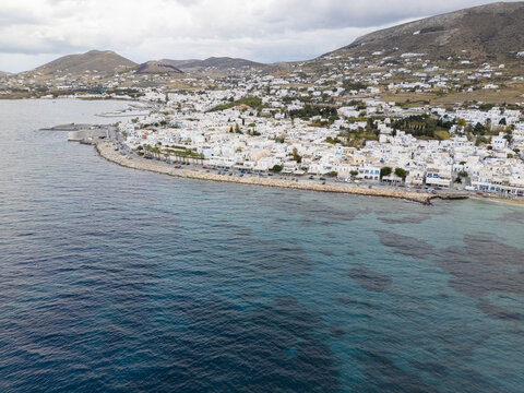 Aerial view of whitewashed buildings nestled against the dramatic coastline, where turquoise waters meet the shore, revealing the town's unique charm, Paros, Paros, Greece.