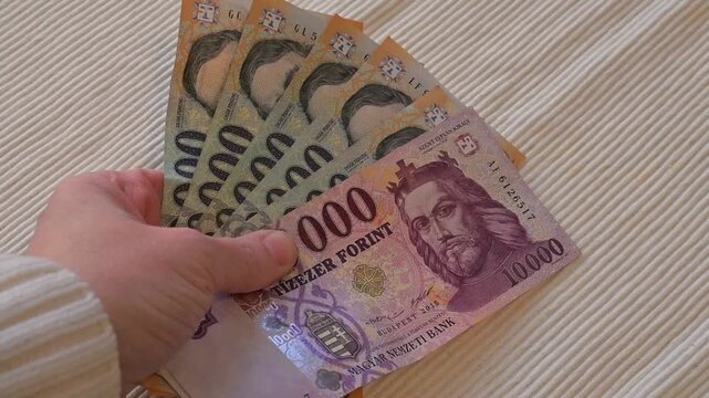 Close-up video of a female hand placing Hungarian forint banknotes onto a table on a white background with Copy Space. Financial concept illustrating payment, budgeting, income, savings, expenses, and