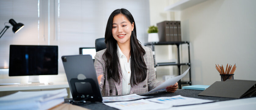 Successful and joyful woman at workplace checking financial reports and contracts. Businesswoman doing paperwork inside office, using tablet. Financier preparing and filling out tax forms
