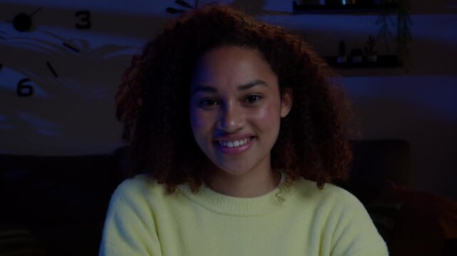 Young Afro woman smiling at camera in a living room at night.