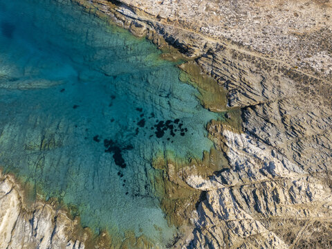 Aerial view of the turquoise waters meet the rugged coastline, creating a mesmerizing contrast of colors and textures, Paros, Paros, Greece.