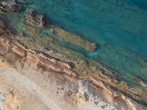 Aerial view of turquoise waters meeting the rugged coastline, creating a stunning contrast of colors and textures along the shore, Paros, Paros, Greece.