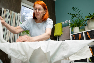 A mature woman carefully arranges a damp shirt on a collapsible dryer rack, spreading it out to avoid creases and ensure it dries smoothly.