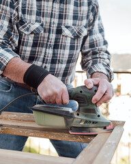 Craftsman. Adult carpenter using an electric sander to smooth an old wooden window. Construction industry, carpentry, housework do it yourself. Restoration.