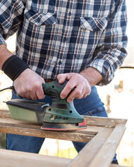 Craftsman. Adult carpenter using an electric sander to smooth an old wooden window. Construction industry, carpentry, housework do it yourself. Restoration.
