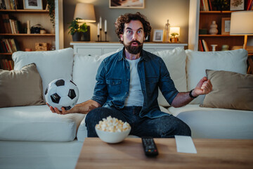 Man intently watching football match on tv at home