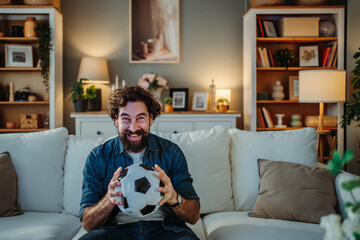 Happy man holding soccer ball watching sports at home