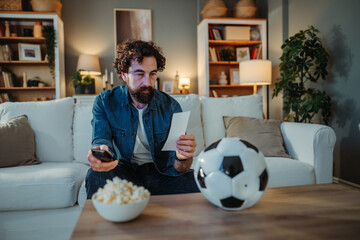 Man holding betting slip watching football match