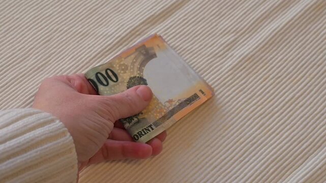 Close-up video of a female hand placing Hungarian forint banknotes onto a table on a white background with Copy Space. Financial concept illustrating payment, budgeting, income, savings, expenses, and