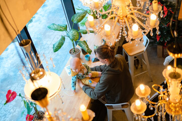 Young father with toddler in arms sitting in cafe. View from above shows warm parenting bond, family values, love and happiness in modern restaurant interior with cozy atmosphere.