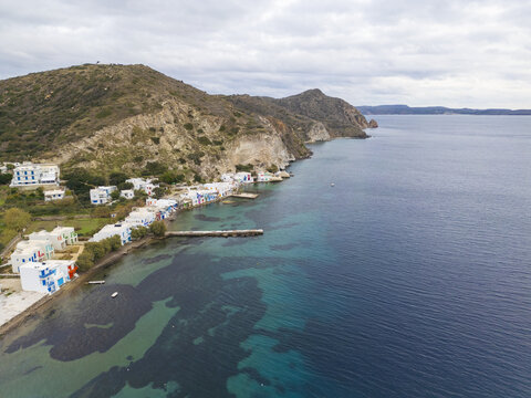 Aerial view of colorful houses nestled along the shoreline, where the land meets the tranquil, deep blue sea, Klima, Milos, Greece.