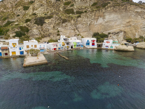 Aerial view of the vibrant, colorful houses of Klima cascade down to the clear turquoise sea, nestled against the rugged cliffs, Klima, Milos, Greece.