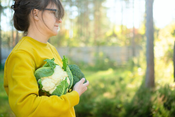 Female farmer holding basket of cauliflower and broccoli at sunset on farm land. Seasonal vegetables, fresh harvest, homegrown produce, healthy food, and nature lifestyle.