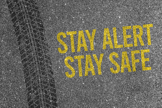Tire track on asphalt background with yellow text Stay Alert Stay Safe. Road safety and traffic awareness.