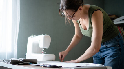 Woman tailor aligning and straightening the textile on her studio worktable, preparing the material for accurate cutting and sewing.