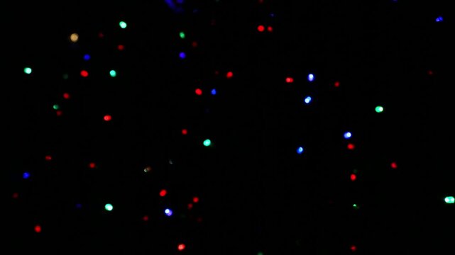Multicolored bokeh light dots float across deep black background, gently drifting and twinkling as particles scatter, fade, and reappear, creating seamless festive abstract motion loop as overlay.