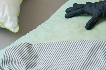 A person wearing a black glove touching a green pillow with dirty yellow stains sweat or saliva in a living room. Conscious home care and sustainable living concept. top view