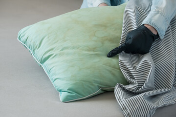 A person wearing a black glove touching a green pillow with dirty yellow stains sweat or saliva in a living room. Conscious home care and sustainable living concept. top view