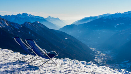 Blue winter cold landscape, calmness and 2 chairs on ski resort during winter seaon and view to mountains and Pinzolo village in Alps