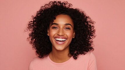 Smiling beautiful woman with curly hair wearing plain pink t-shirt standing against solid color background in studio setting. Natural and fresh portrait concepts.