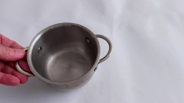 An empty stainless steel pot with side handles sits on a white surface - highlighting clean kitchenware, simple composition, and a calm moment in culinary preparation