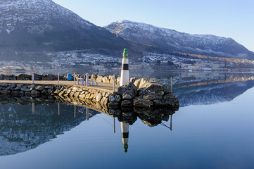 Scenic pier with lighthouse at dawn reflecting in still water with mountains in the background