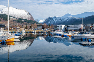 Scenic view of a marina with boats on calm water and mountains in the background during daylight hours in a coastal town