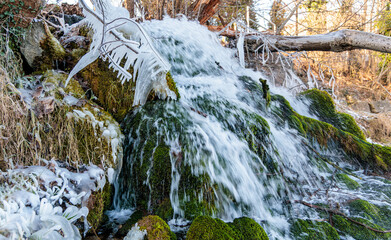 Close-up of a small waterfall in winter with crystal clear icicles hanging from mossy rocks and branches. Scenic nature photography 
