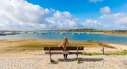 woman sitting on bench enjoying view of the sea and fishing boat, Travel in Portugal, Algarve, city of Alvor