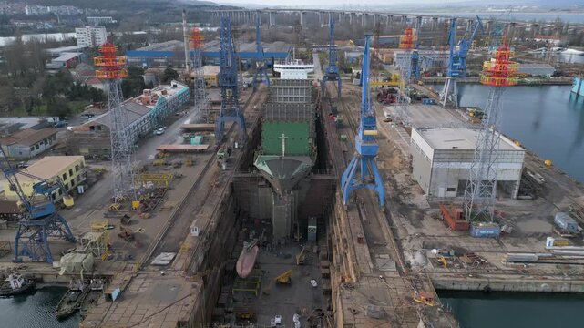 Aerial view of a ship repair yard with dry docks, cranes, and cargo vessels in an industrial port. Large shipyard infrastructure, maritime industry, logistics and repair operations by the water